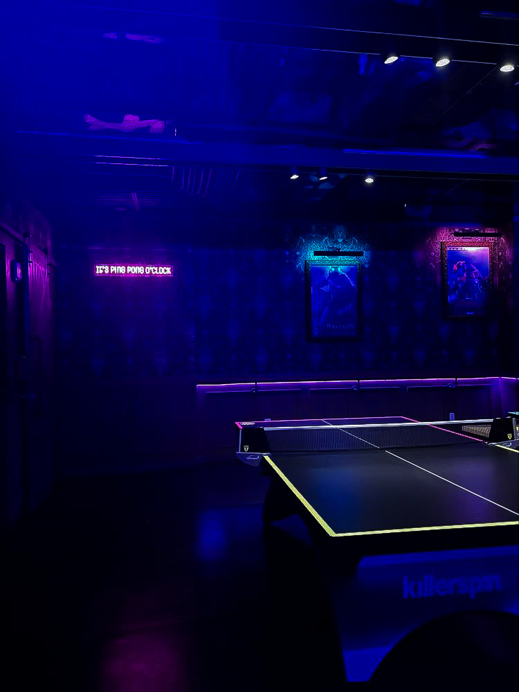 Glowing ping pong table with a neon sign reading it's ping pong o'clock